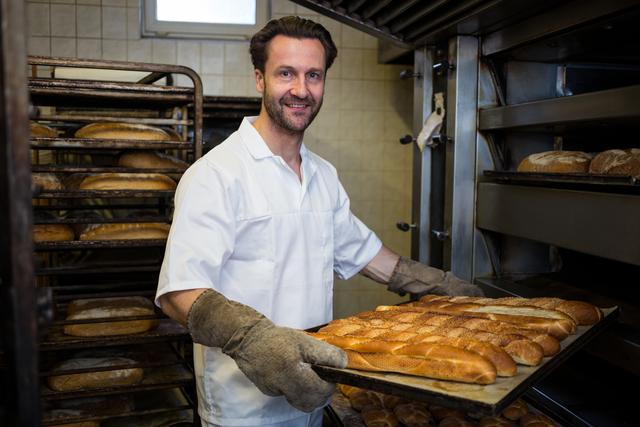 Portrait of smiling baker removing baked buns from oven