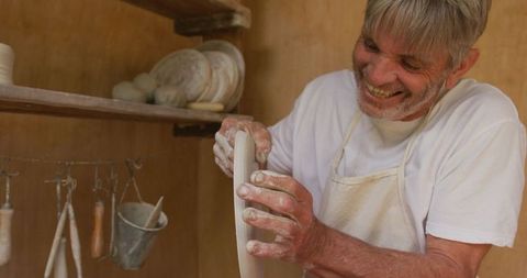 Senior man joyfully shaping pottery in workshop