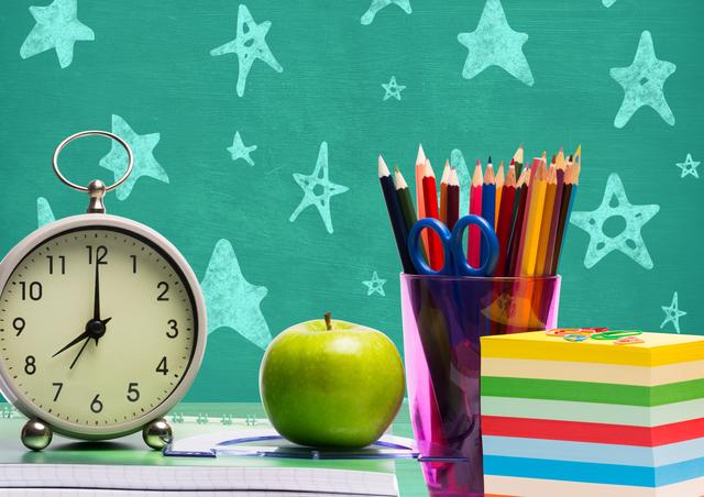 Various stationeries, alarm clock and apple against chalkboard