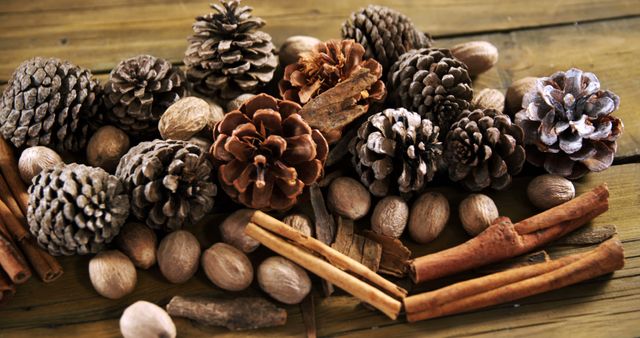 A variety of pine cones, cinnamon sticks, and nuts are arranged on a wooden surface, creating a warm and rustic ambiance. These elements are often associated with autumnal and winter decorations, evoking a sense of coziness and natural beauty.