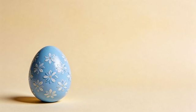 Pastel blue easter egg featuring white daisy motifs on minimal beige background