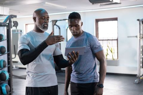 African american trainer coaching client with tablet in modern gym for workout planning