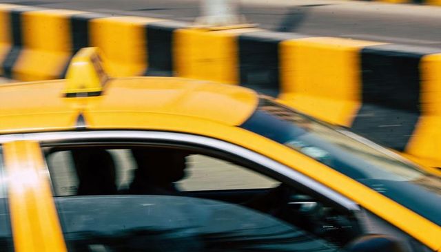 Yellow taxi passing with roof sign and driver silhouette blurred motion on city road
