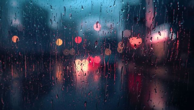 Rain-splashed window blurring neon city lights, moody wet street bokeh at night