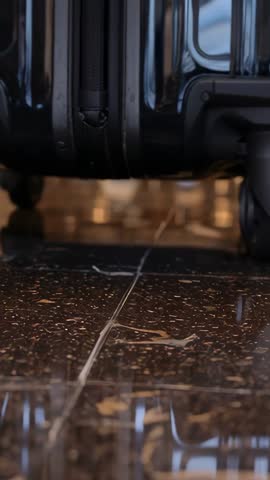 Vertical Close-Up Showing Suitcase Wheels Rolling on Polished Tile Floor with Soft Glow