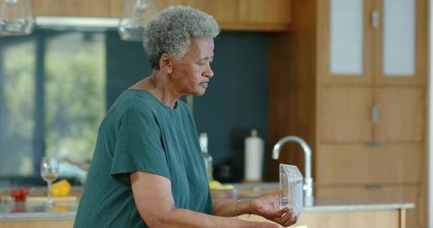 Senior african american woman inspecting clear plastic clamshell at modern kitchen counter