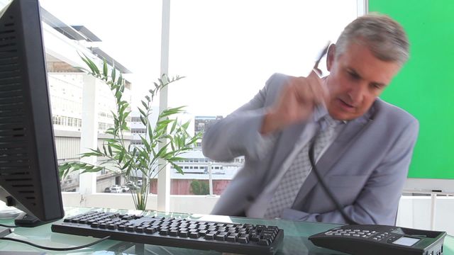 Businessman looking frustrated while ending a phone call in a modern office environment. Ideal for illustrating concepts of workplace stress, communication challenges, or business frustrations. Useful for articles, presentations, or advertisements focused on professional settings and stress management.