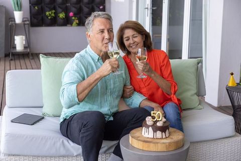 Mature couple celebrating 50th milestone on terrace toasting white wine with chocolate cake