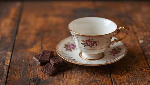Vintage floral china teacup with gold handle on rustic wooden table with dark chocolate