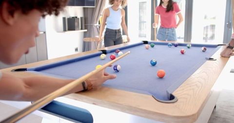 Friends playing pool at modern blue-felt table in bright contemporary game room