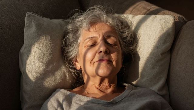 Senior woman relaxing on sunlit sofa with eyes closed, calm intimate moment at home