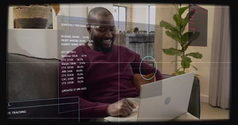 Smiling man checking sales metrics on laptop with hud overlay, remote work on sunlit sofa