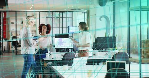 Three professional women discussing tablet and digital design in modern open-plan office