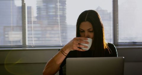 Focused Businesswoman Drinking Coffee While Working with Laptop in Office