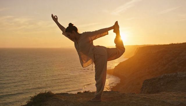 Sunset yoga practicing on ocean cliff, woman balancing in natarajasana silhouette