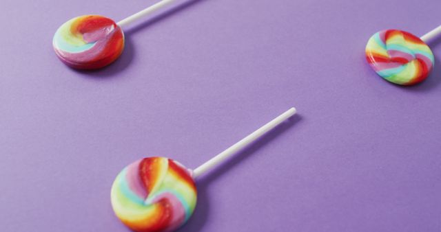 Vibrant rainbow swirl lollipops showcased on a purple background, perfect for adding a pop of color to party invitations, dessert menus, or confectionery advertisements. Ideal for themes involving fun, candy, and celebrations.