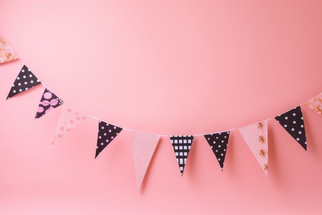Colorful fabric bunting garland featuring various patterns, hanging against a soft pink background. Ideal for festive events, party decorations, invitations, and greeting card designs. Can also be used in home decor, photography backgrounds, and DIY craft tutorials.
