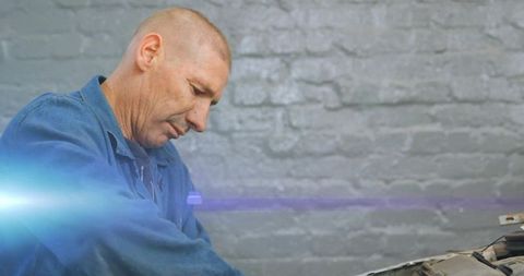 Mechanic Inspecting Car Engine Under Open Hood Garage Workshop with Bluish Lens Flare