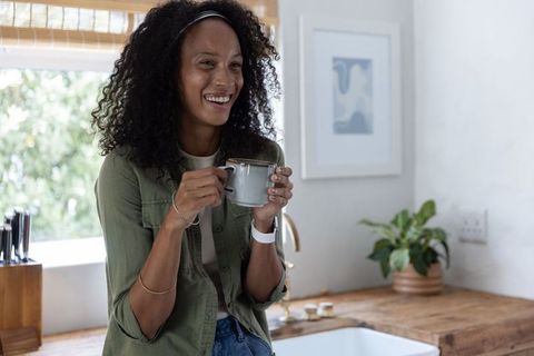 Relaxed african american woman enjoying morning coffee in bright kitchen with natural light