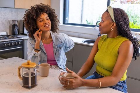 African american women chatting over coffee at modern marble kitchen island, cozy morning