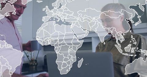 Mature couple collaborating remotely in kitchen with global map overlay on laptop
