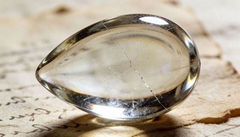 Teardrop crystal lens on aged parchment with hairline cracks macro reflection
