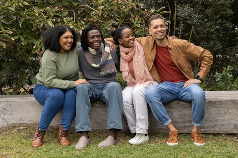 Friends sitting together on park bench linking arms and laughing