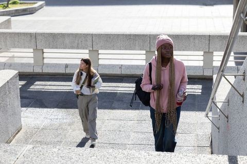 Diverse female students walking up stairs carrying backpacks notebooks and coffee on sunlit campus