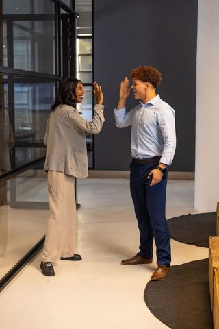 Diverse coworkers giving high-five in modern office corridor celebrating teamwork