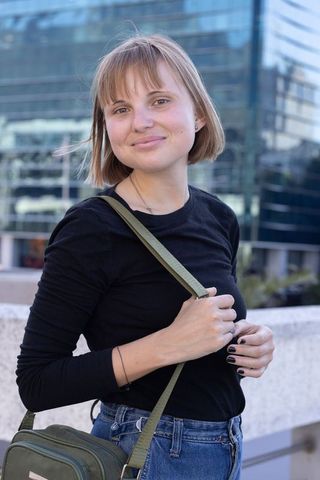 Young woman smiling in black top and jeans with olive-green crossbody bag on urban terrace
