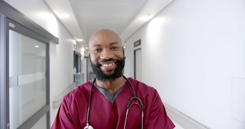 Smiling Male Doctor Wearing Scrubs in Hospital Corridor