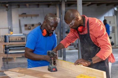 African american carpenters measuring and drilling wood plank in busy workshop