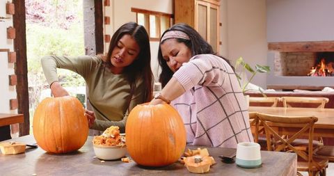 Multiracial family carving pumpkins for halloween in cozy kitchen