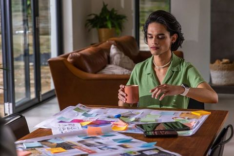 Young asian designer reviewing moodboards at home table holding coffee, planning project