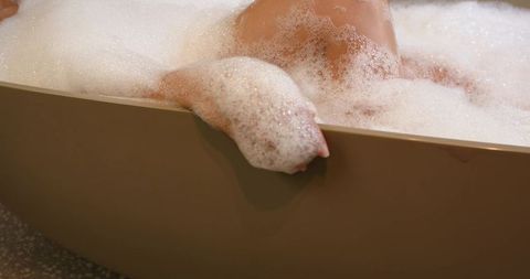 African american woman relaxing in bubble bath with arm resting on freestanding tub rim