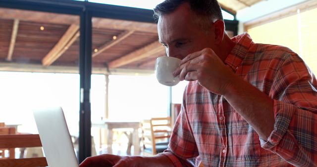 Man drinking coffee while working on laptop in cozy cafe - Download Free Stock Images Pikwizard.com