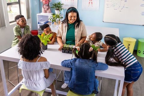 Elementary teacher guiding students planting seedlings during classroom science lesson