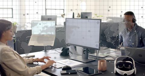 Team collaborating in open-plan office using multiple monitors, vr headset and data charts