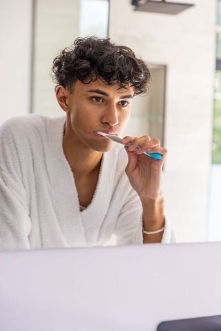 Young Male in Bathrobe Brushing Teeth in Modern Bathroom