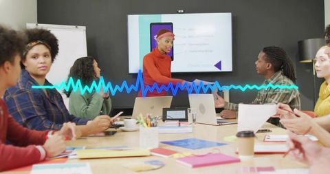 Team collaborating in creative meeting with presenter gesturing to screen and waveform