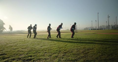 Baseball team practicing fielding drills on early morning dewy field