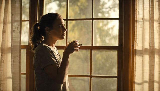 Woman gazing through wooden paned window holding cup at golden hour, contemplative moment