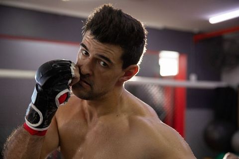 Sweaty male mma fighter training in caged gym showing focus and intensity