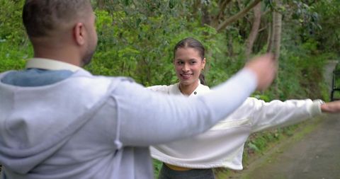 African american man and asian woman reaching arms outdoors on lush tree-lined path
