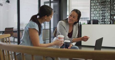 Two Businesswomen Collaborating with Laptops Over Coffee in Modern Office