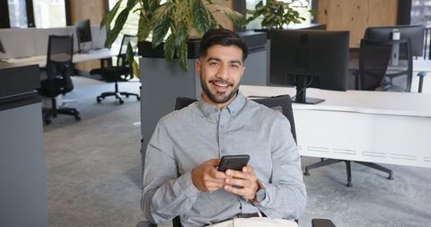 Smiling Professional Male in Modern Office Holding Smartphone