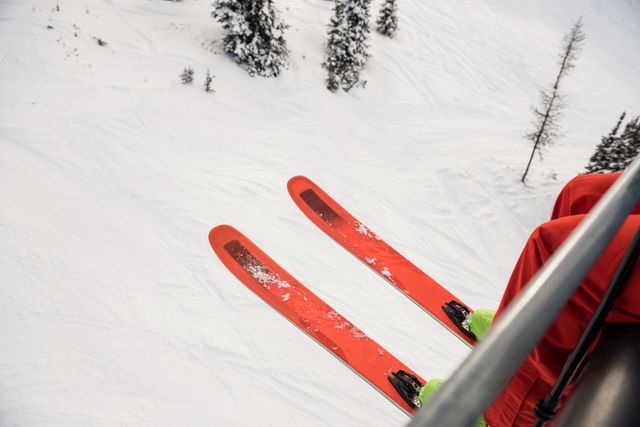 Skier riding a ski lift with bright red skis, surrounded by a snowy mountain landscape. Ideal for use in travel brochures, winter sports promotions, adventure tourism advertisements, and outdoor activity blogs.