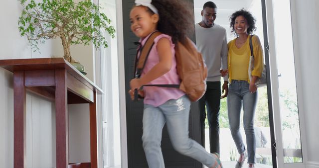This image captures a joyful family moment where a young daughter runs into the home, expressing excitement. The parents follow with smiles, portraying a cheerful and welcoming environment. Great for illustrating family lifestyles, real estate promotions, parenting blogs, or advertisements focusing on home or family products.