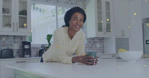 Smiling woman leaning on white kitchen island holding teal mug in bright modern kitchen