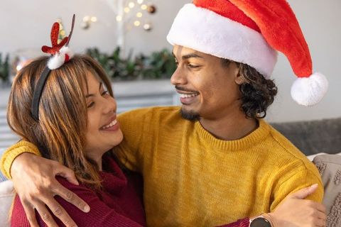 Couple sharing cozy holiday hug wearing santa hat and reindeer antlers on couch